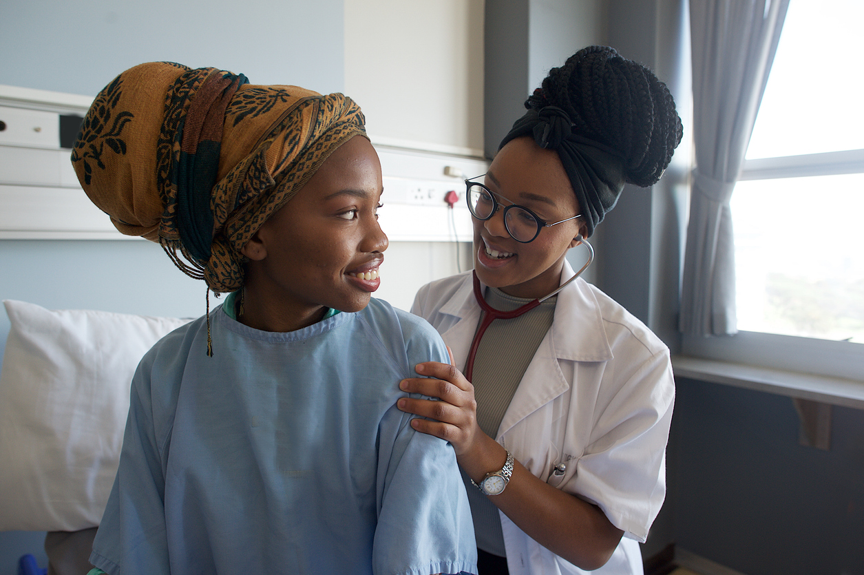 Young Female Doctor listening with stethoscope on patient's back smiling at the doctor