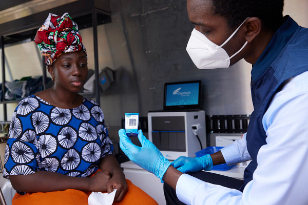 Two women, wearing lab coats and safety gear, operating sequencing equipment in a lab.